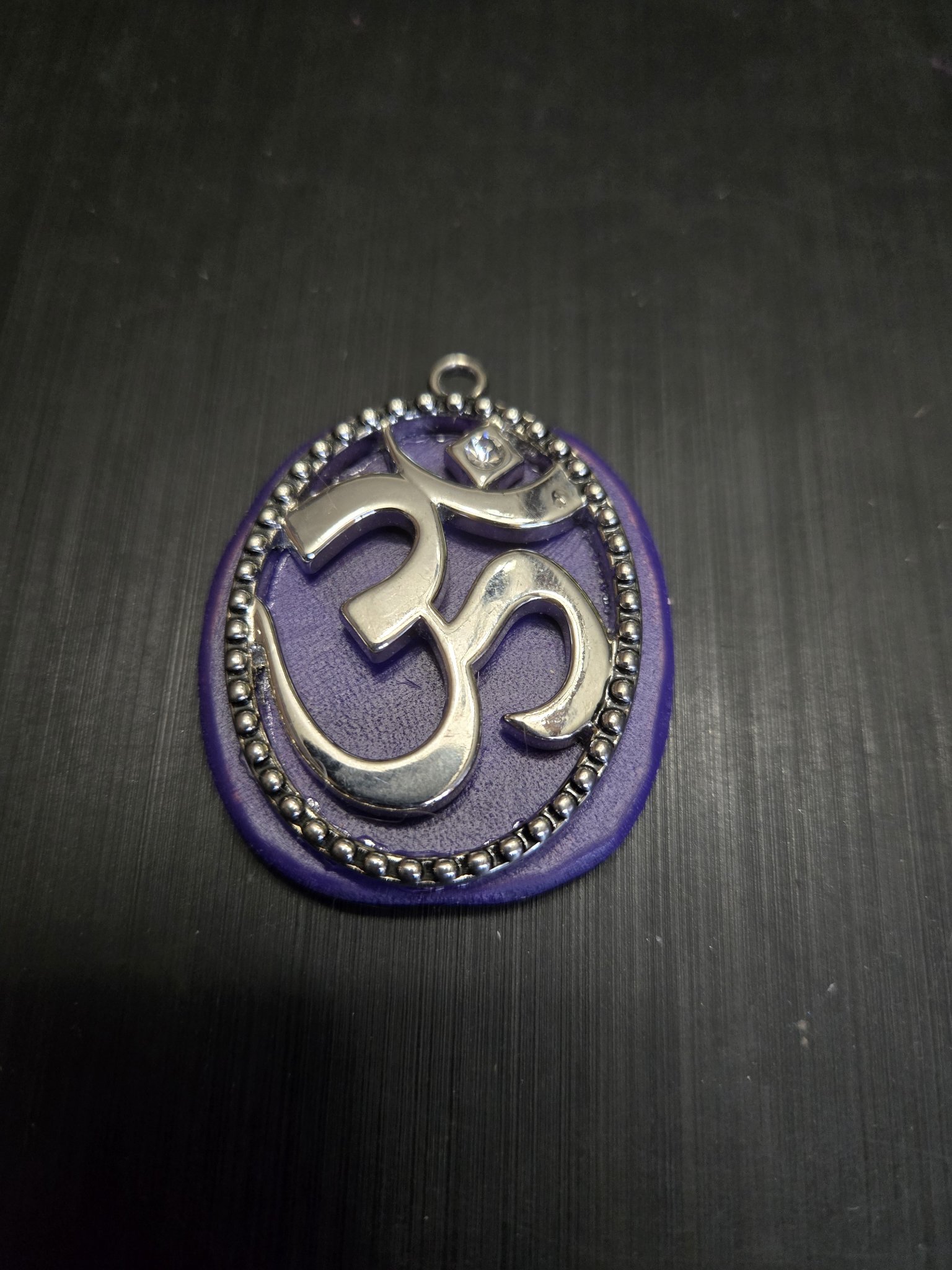 Close-up of stock 151 showing the silver-tone Om symbol, crystal accent, and beaded oval frame