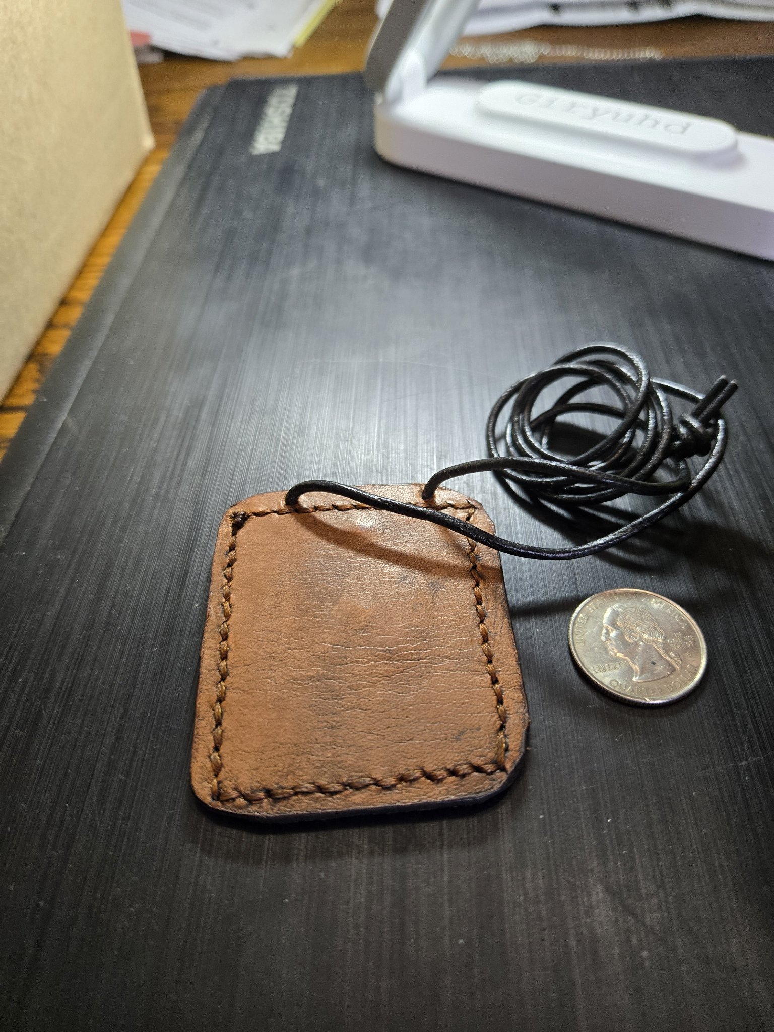Back of stock 159 hand-sewn brown leather pendant beside a quarter