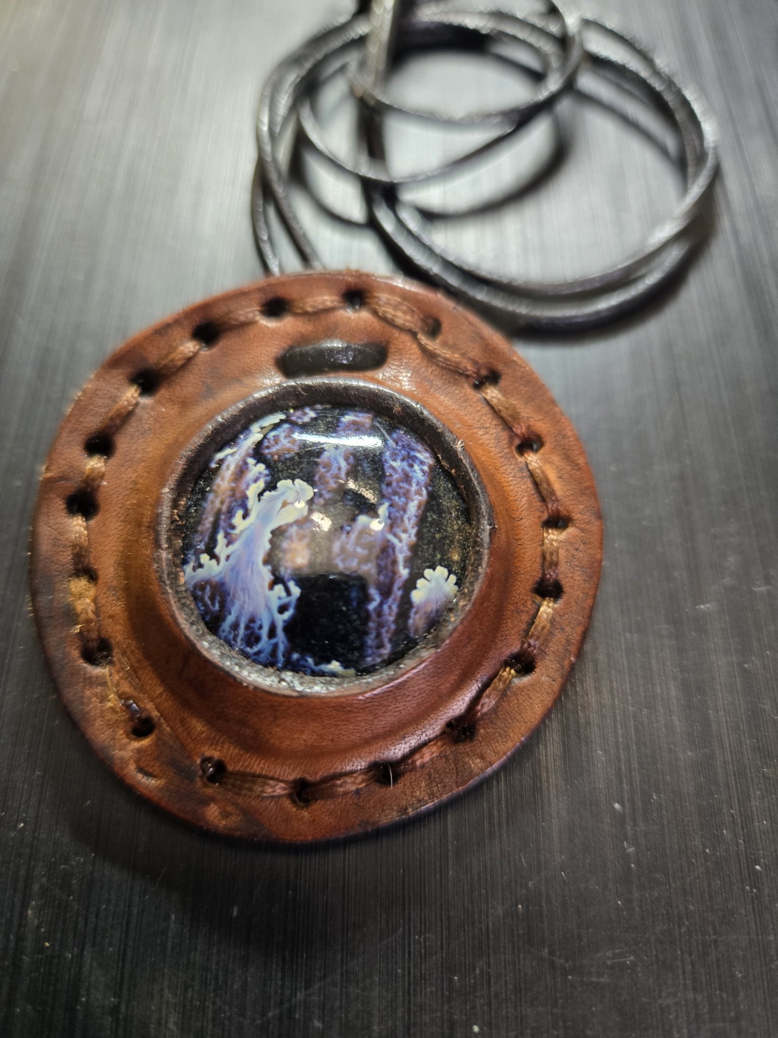 Front close-up of stock 160, a hand-sewn round brown leather pendant with a blue and white ceramic stone cabochon