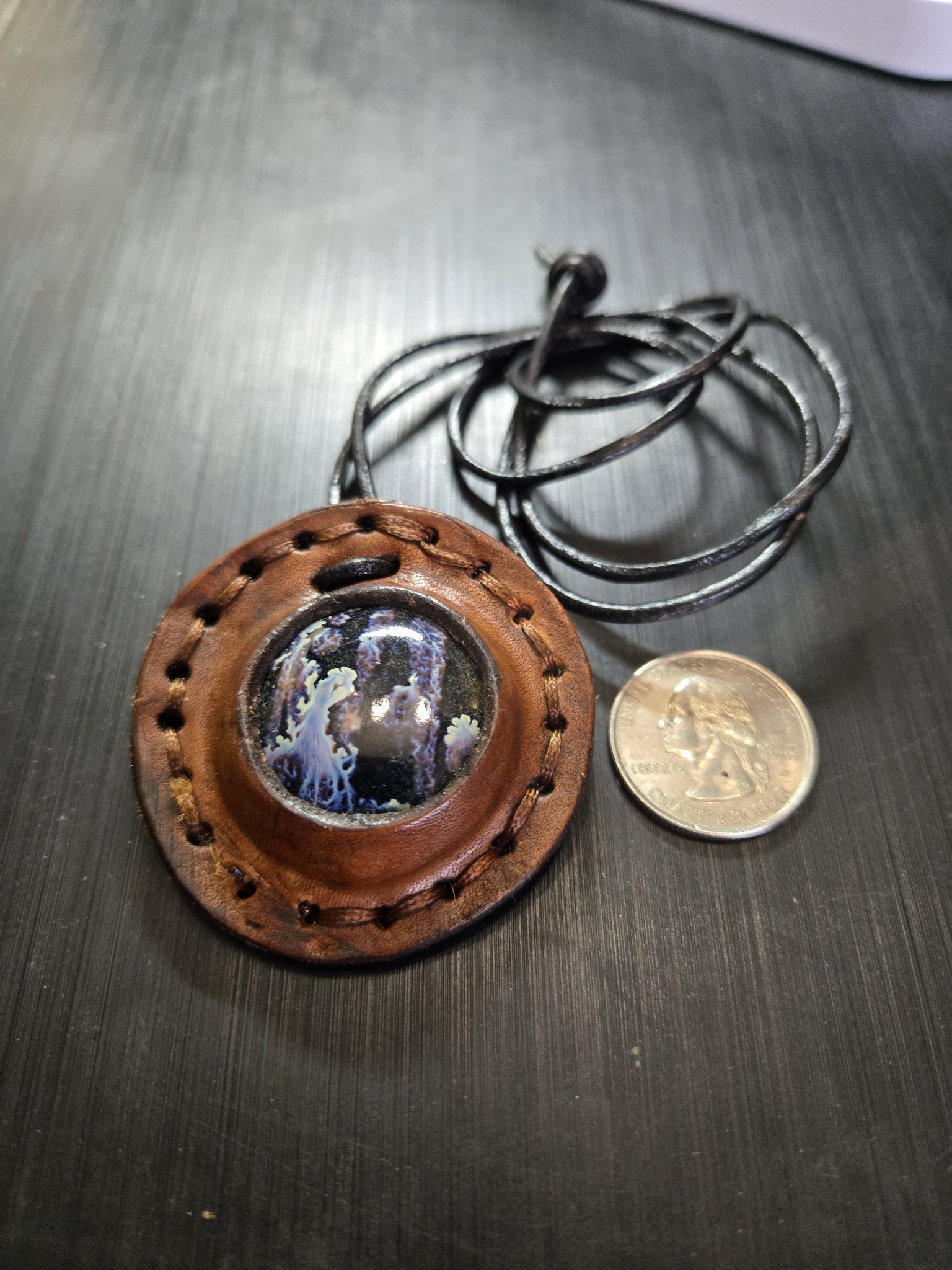 Front of stock 160 beside a quarter showing the round leather pendant is approximately two inches across