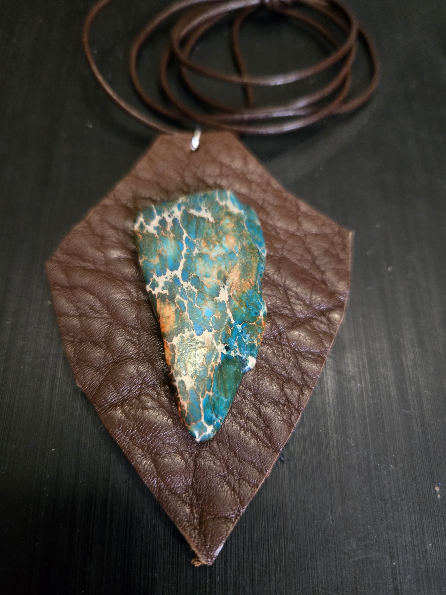 Front close-up of stock 164, a shield-shaped brown buffalo leather pendant with a blue and brown agate stone cabochon