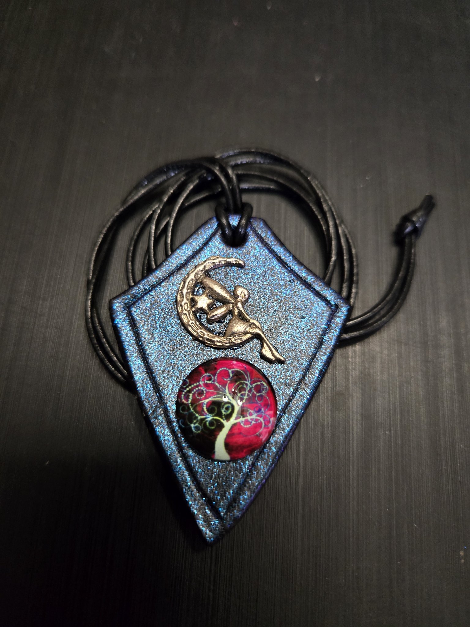 Stock 165 diamond-shaped blue iridescent leather pendant with a silver-tone fairy on crescent moon charm, tree-of-life cabochon, and 30-inch black leather cord necklace