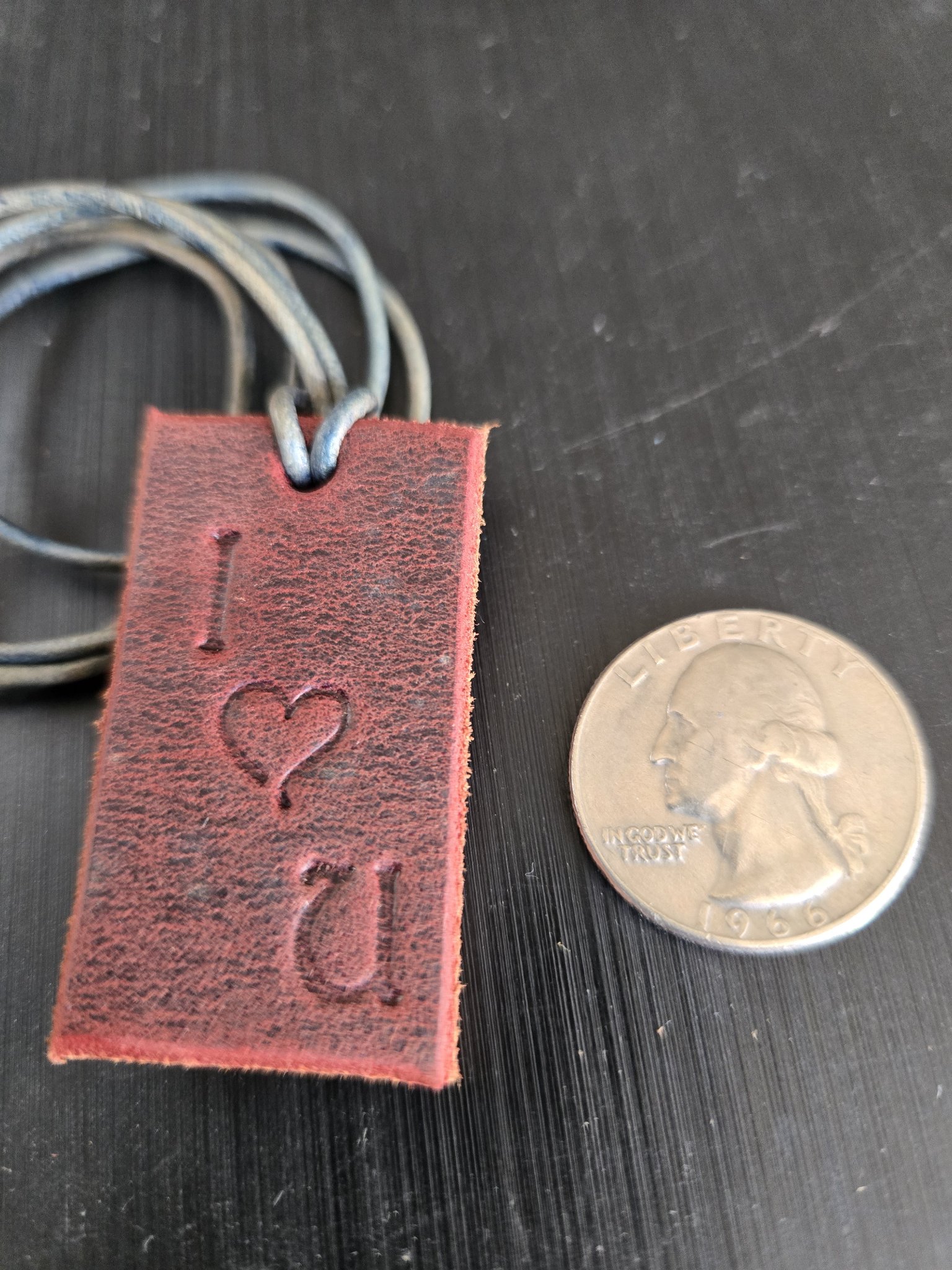 Front view of stock 177 I love you saddle leather pendant beside a quarter for scale