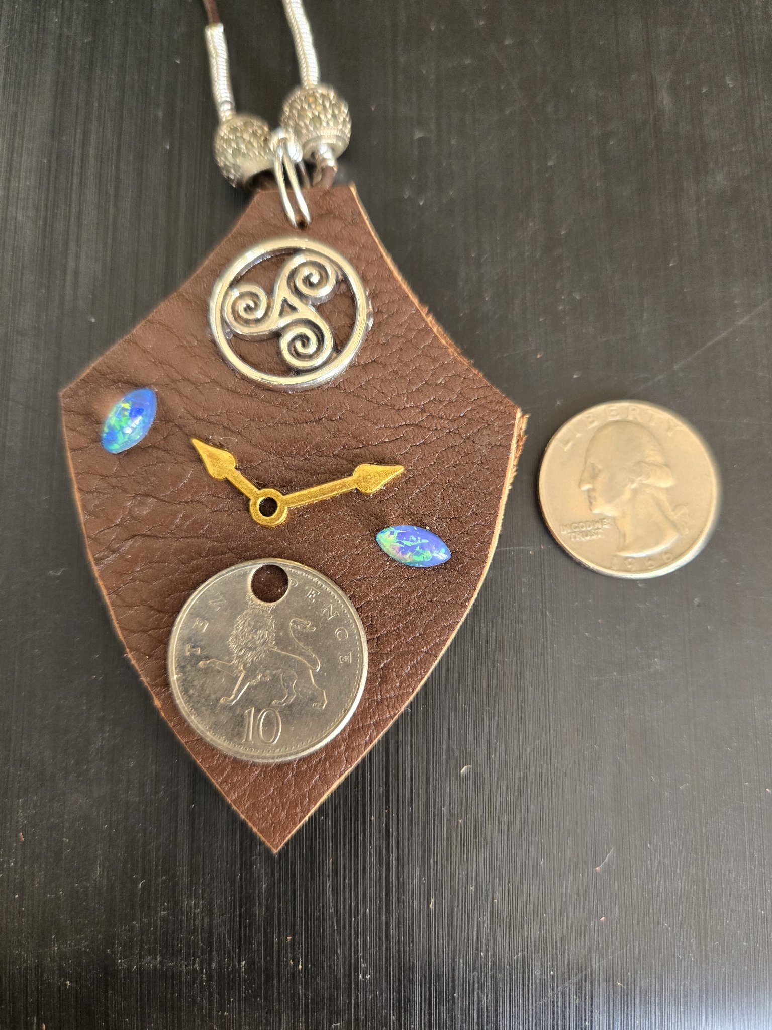 Front of stock 178 trinity shield buffalo leather pendant beside a quarter for scale