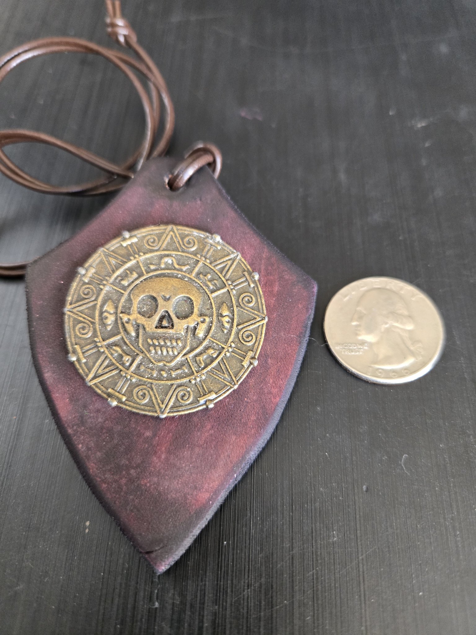 Front of stock 179 Aztec skull shield leather pendant beside a quarter for scale