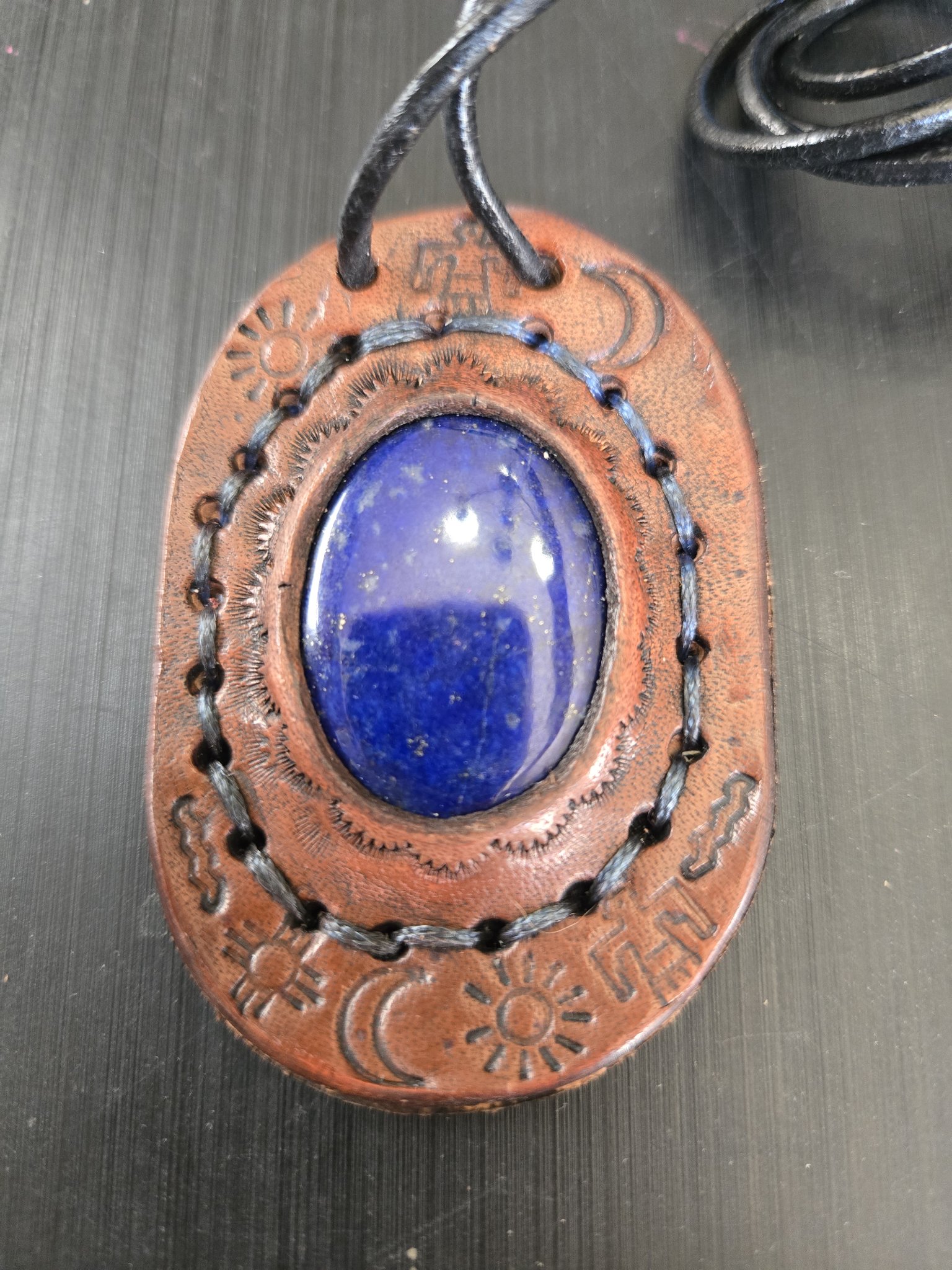 Stock 181 hand-sewn oval brown leather pendant with an oval lapis lazuli stone cabochon and stamped sun, moon, and zia sun symbols, shown in a front close-up