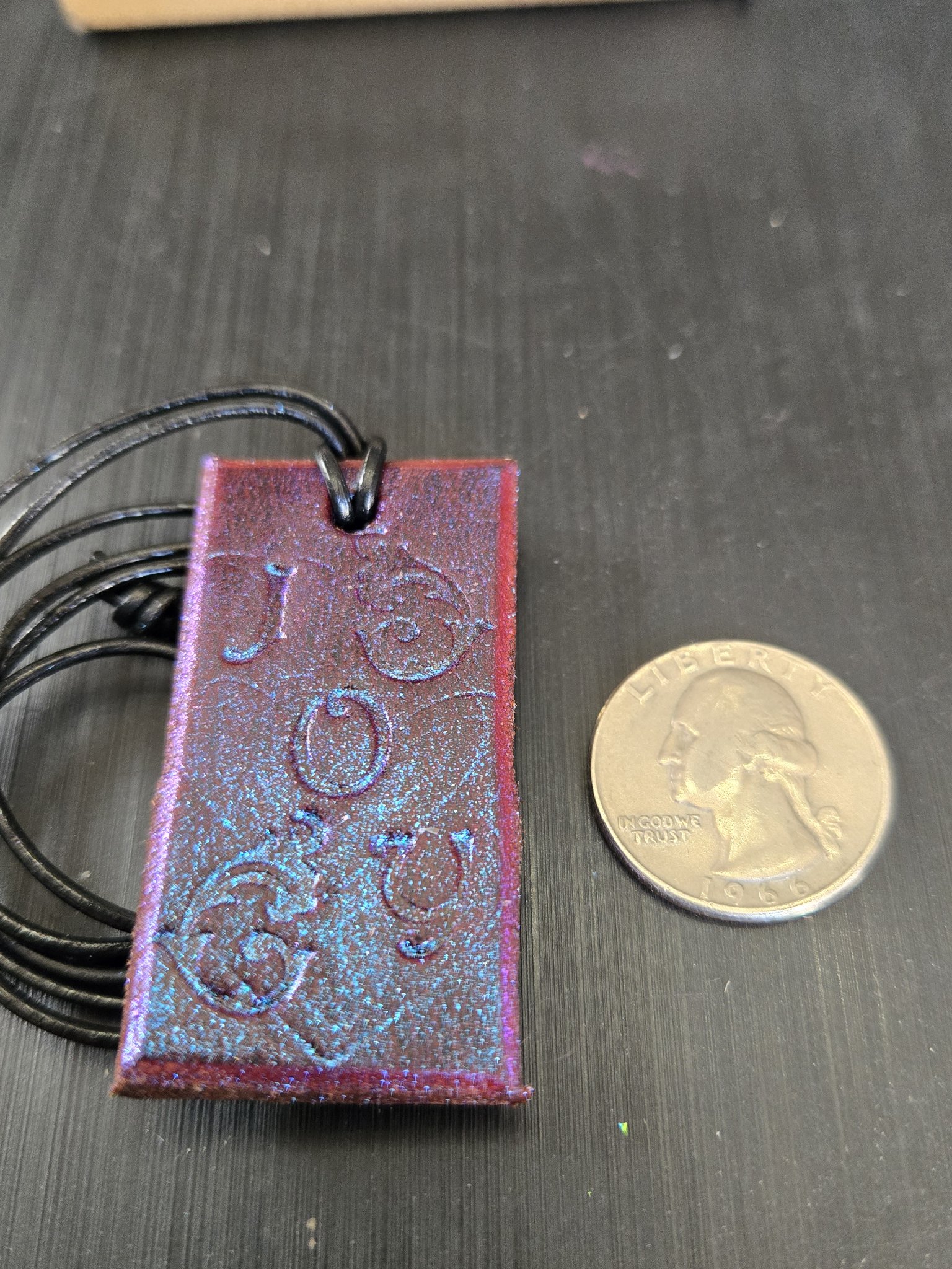 Front of stock 185 JOY saddle leather pendant beside a quarter for scale