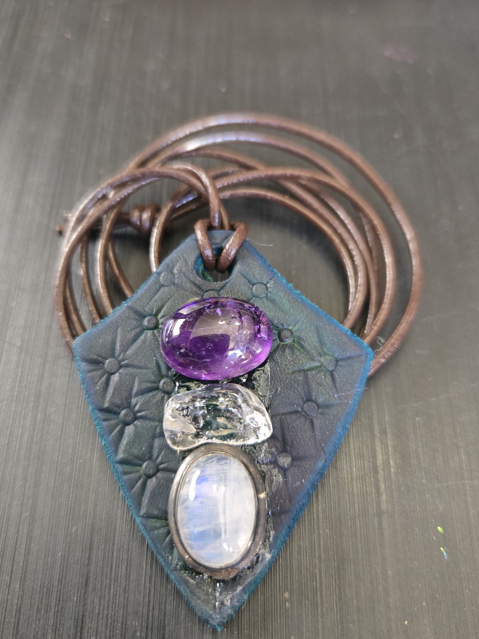 Stock 187 diamond-shaped hand-stamped dark blue leather pendant with an oval amethyst, clear quartz, and oval moonstone in a sterling silver bezel, shown in a front close-up