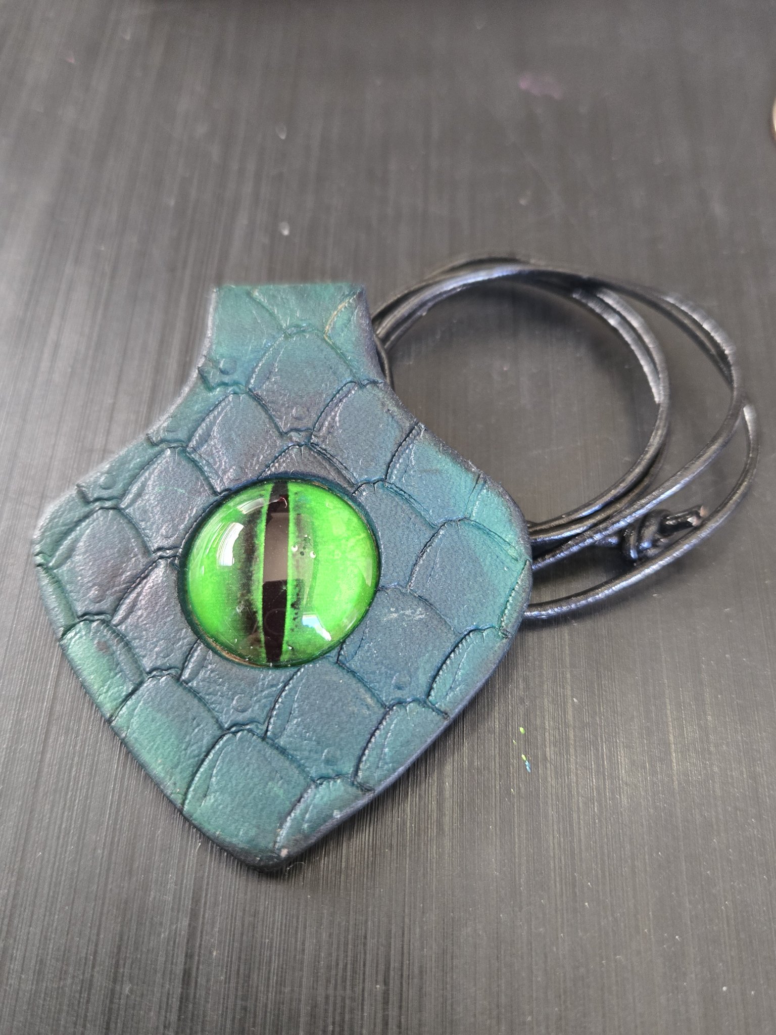 Stock 188 diamond-shaped green leather pendant with dragon scale stamping and a green dragon eye glass cabochon, shown in a front close-up