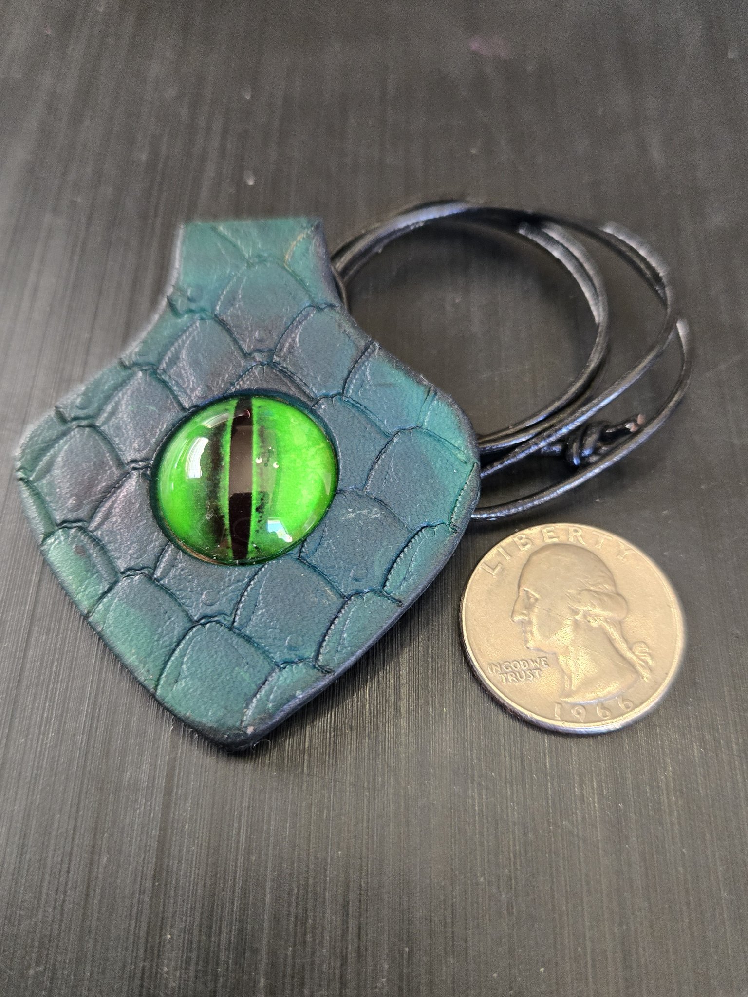 Front of stock 188 green dragon eye leather pendant beside a quarter for scale