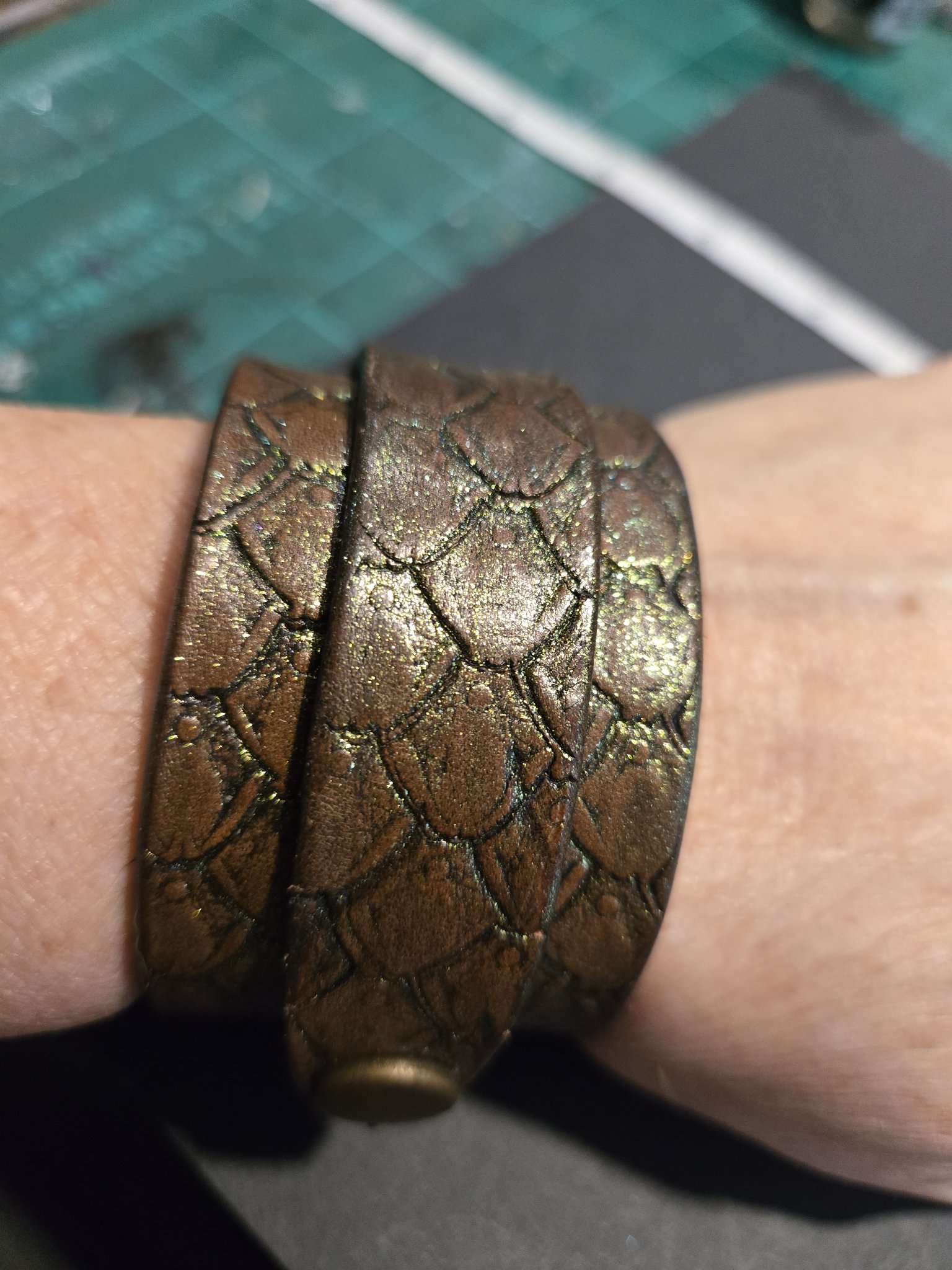 Stock 223 dragon scale leather cuff with a gold and green shimmer, shown on a wrist