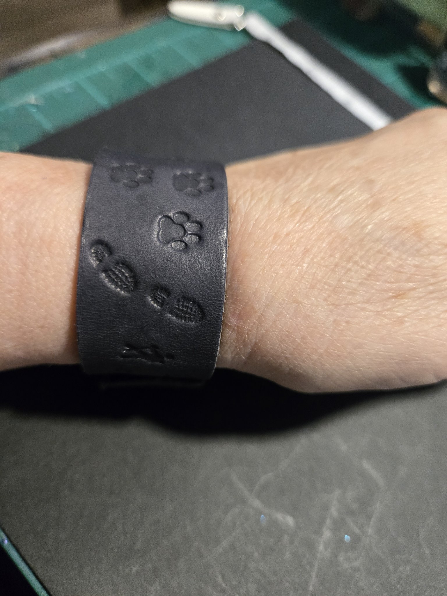 Stock 228 black leather bracelet hand-stamped with dog paw prints and boot prints, shown on a wrist