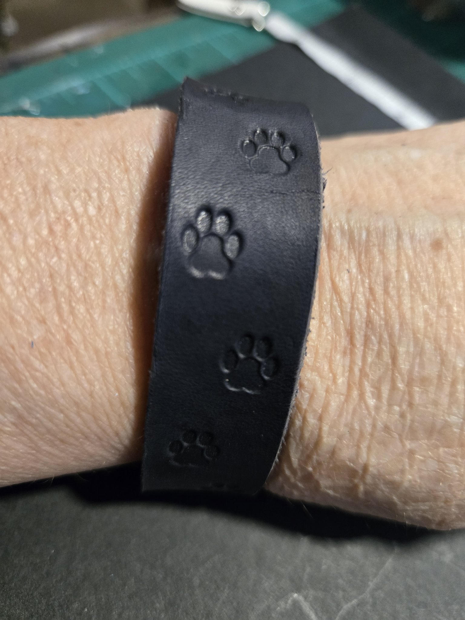 Stock 229 black leather bracelet hand-stamped with dog paw prints, shown on a wrist
